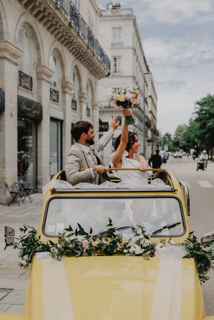 mariés lèvent le bouquet de fleurs debout dans leur voiture jaune pour leur mariage au Pays Basque